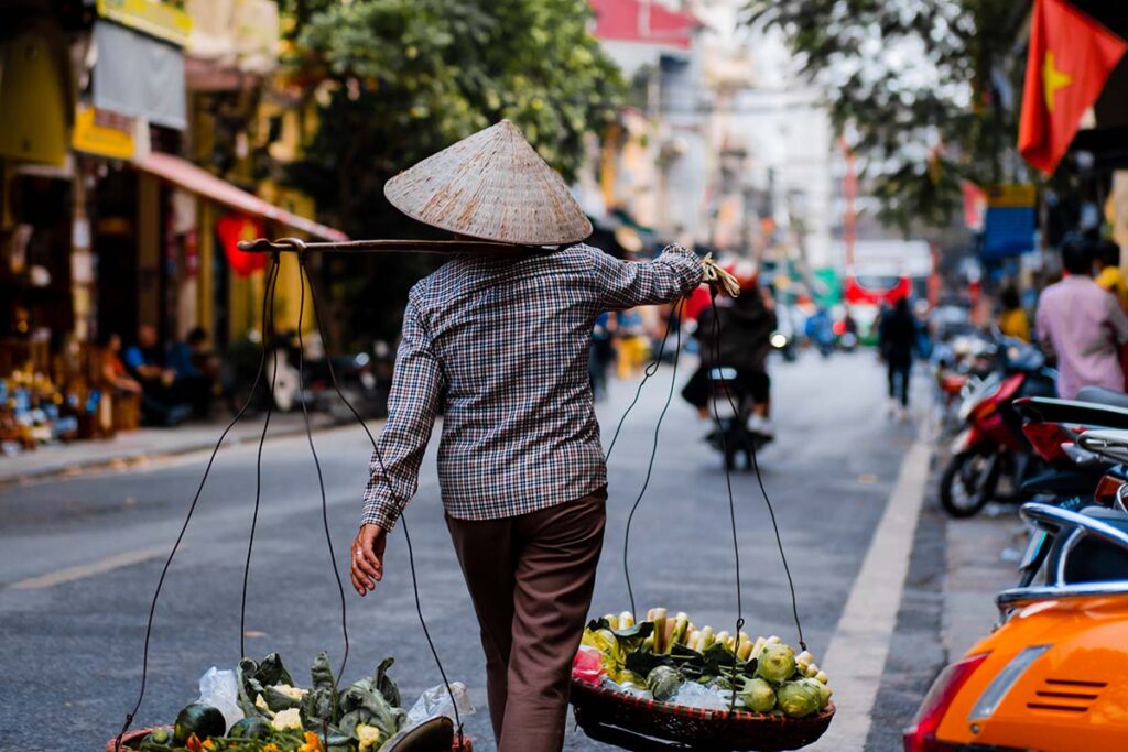 Einheimischer trägt Waren in Körben durch das alte Viertel von Hanoi.