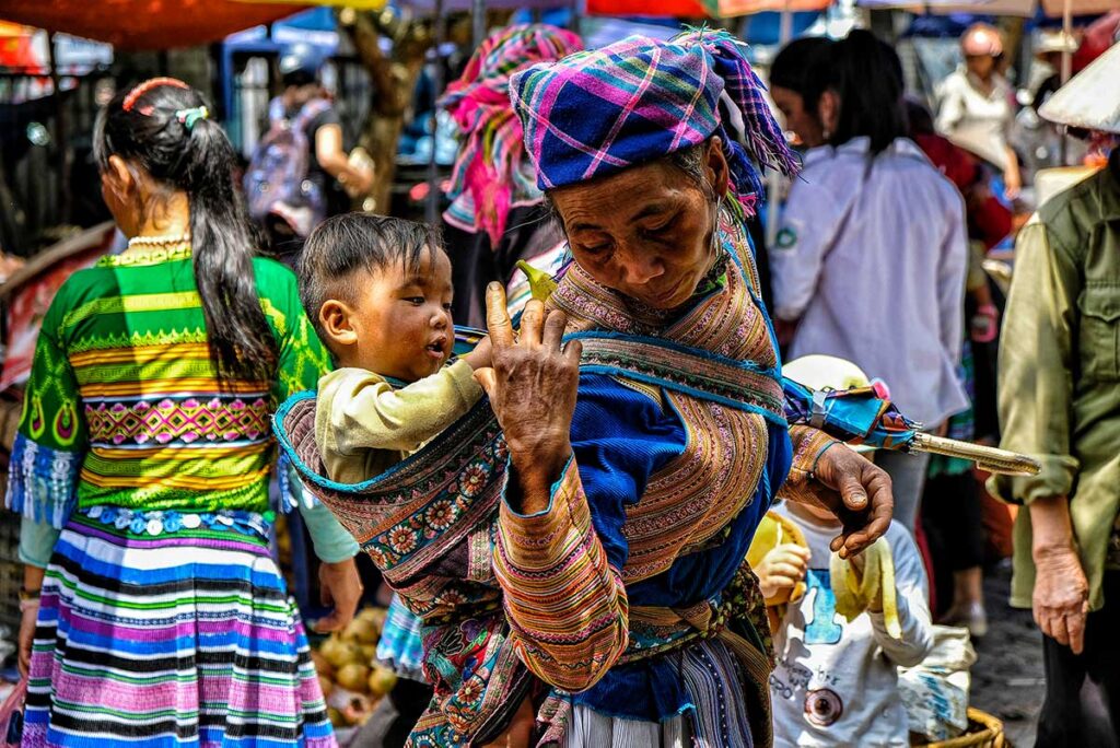 Ethnische Frau trägt ein Baby auf dem Bac Ha-Markt