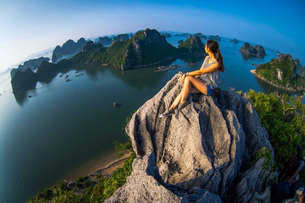 Alleinreisende Frau sitzt auf einem Felsen am Aussichtspunkt des Berges Bai Tho über der Halong-Bucht