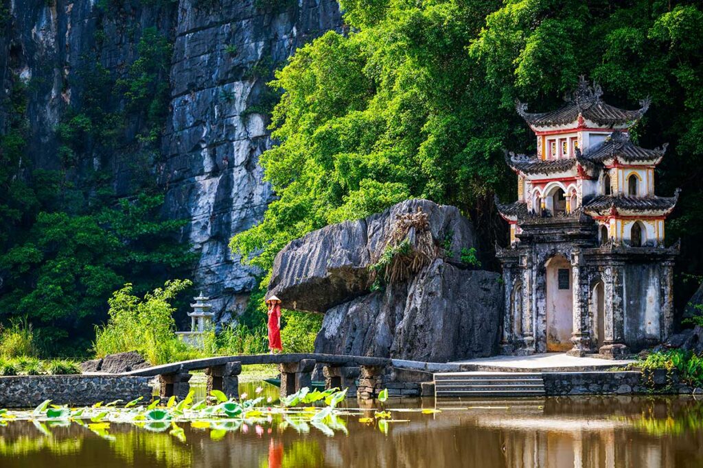 Frau im roten Kleid geht über eine Steinbrücke über den Lotusteich an der Bich-Dong-Pagode in Ninh Binh