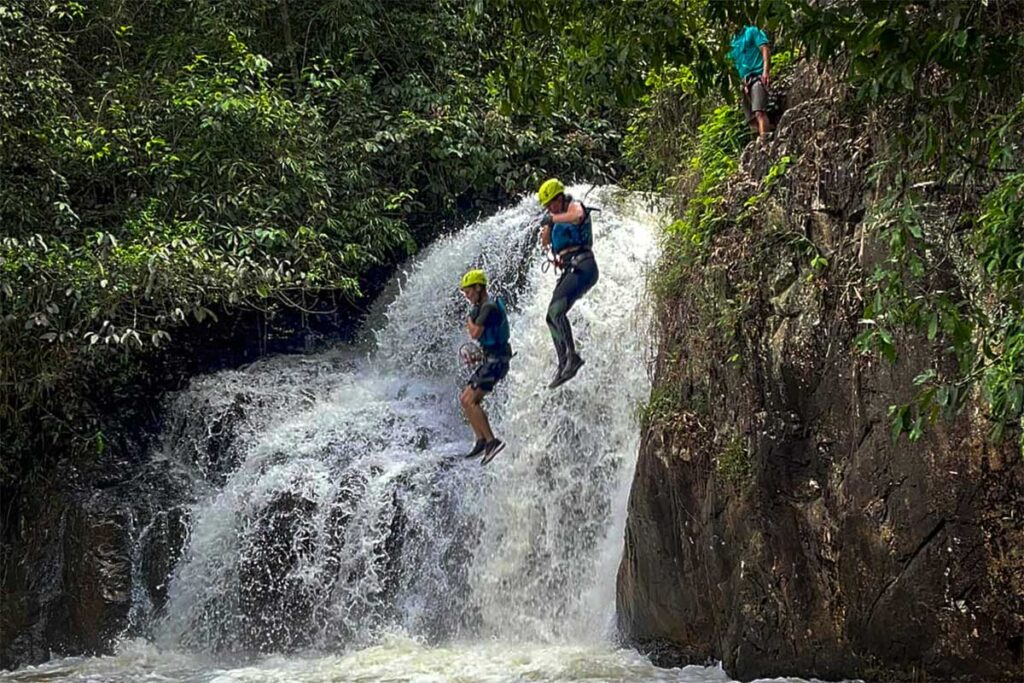 Zwei Personen springen beim Canyoning in Dalat von einer Klippe