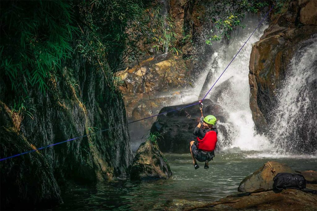 Ein Mann, der beim Canyoning in Dalat mit der Seilrutsche von einem Wasserfall über einer Schlucht herabsaust