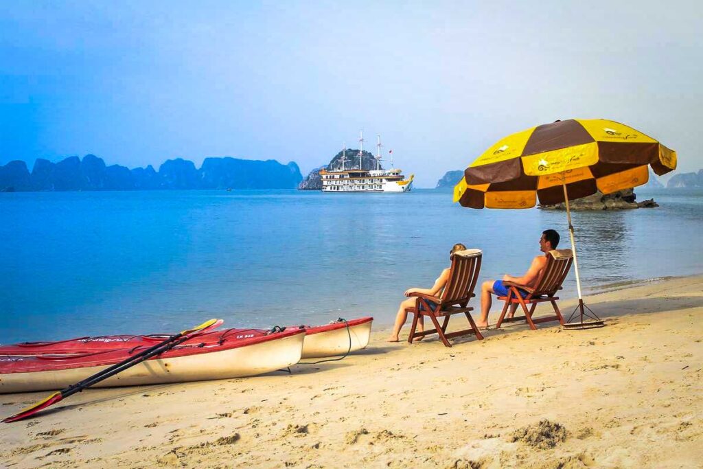 Zwei Touristen sitzen an einem abgelegenen Strand mit Kajaks neben ihnen in der Bucht von Bai Tu Long in Vietnam