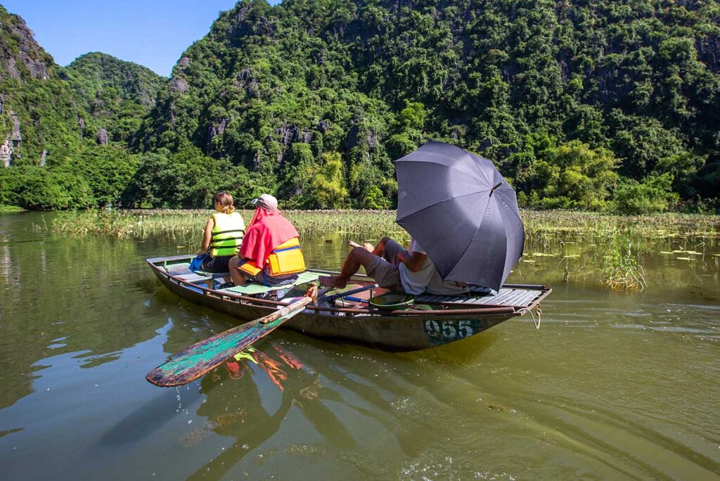 Ein Einheimischer benutzt sein Heck, um ein kleines Ruderboot mit Touristen durch Tam Coc in Ninh Binh zu treiben