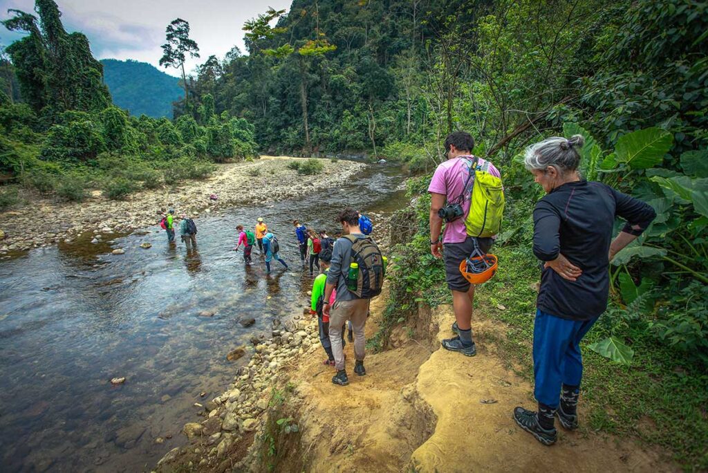 Eine Gruppe von Reisenden wandert durch den Dschungel des Phong Nha Nationalparks und überquert einen kleinen Bach auf dem Weg zum Eingang der Hang Son Doong Höhle.