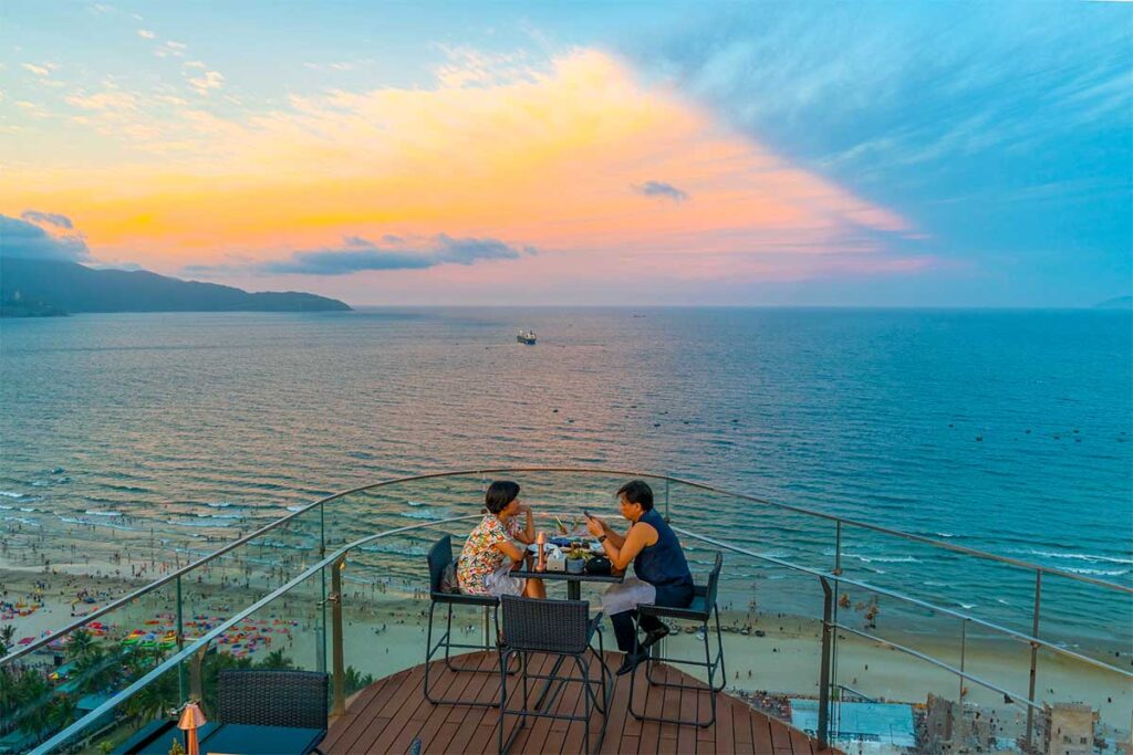 Zwei Personen sitzen in der Sky 21 Bar - Eine Bar auf dem Dach am My Khe Beach mit atemberaubendem Blick auf das Meer und den Strand im Hintergrund