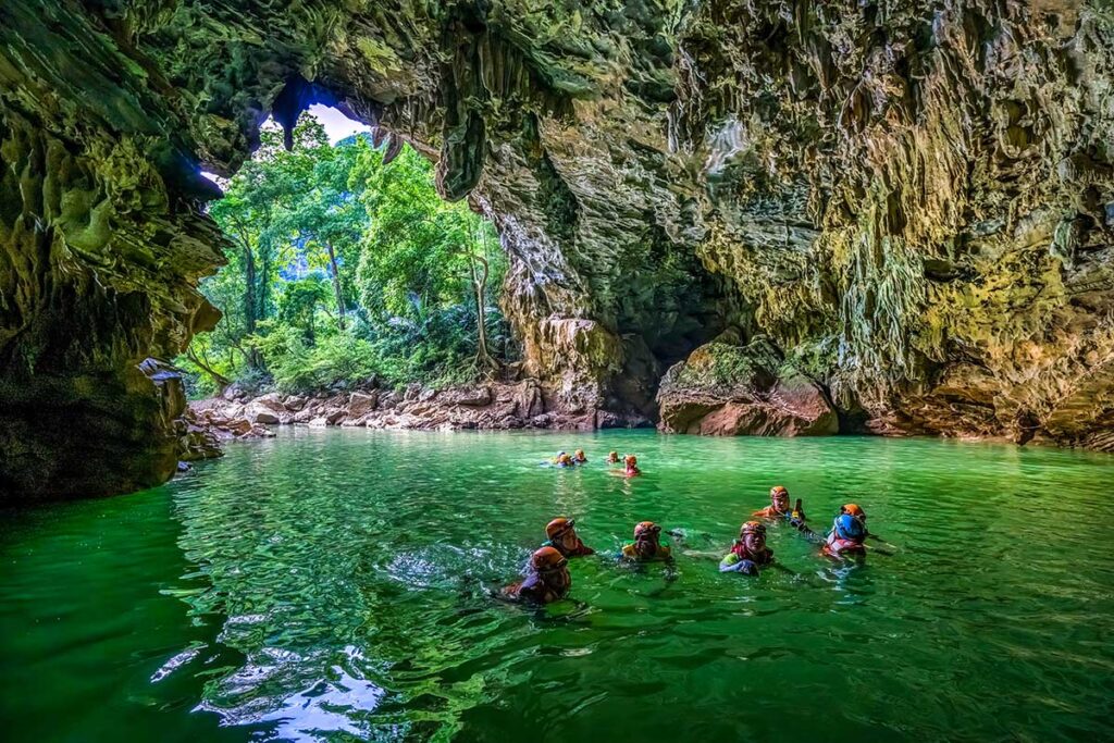 Reisende auf einer Höhlentour schwimmen in einem unterirdischen Fluss des Tu Lan-Höhlensystems im Phong Nha-Nationalpark