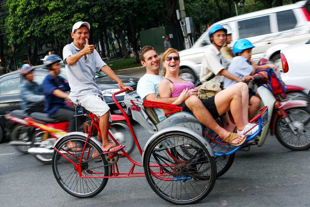 Ein Paar sitzt in einem traditionellen Cyclo und ein Einheimischer fährt sie während ihres Urlaubs in Vietnam durch Hanoi.