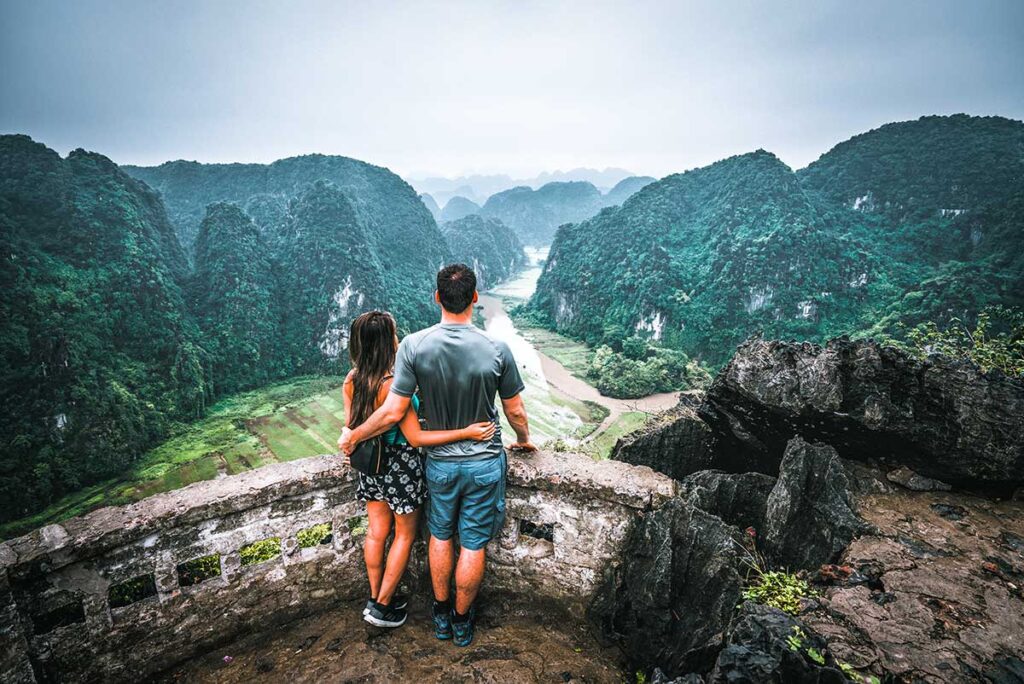 Während eines romantischen Urlaubs in Vietnam halten sich ein Mann und eine Frau fest und genießen von der Mua-Höhle aus den Blick über die Reisfelder von Tam Coc