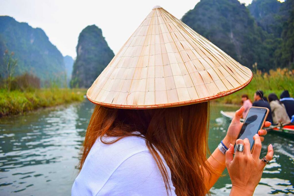 Eine junge Frau nutzt ihr Telefon mit einer lokalen vietnamesischen SIM-Karte, um Fotos von ihrem Vietnam-Urlaub zu senden