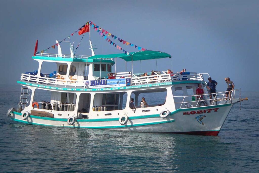 Tauchboot des Flipper Diving Clubs vor Anker auf dem klaren Wasser bei Phu Quoc mit Tauchern an Bord — der Flipper Diving Club ist eine der bekanntesten Tauchschulen für alle, die bei Phu Quoc tauchen möchten
