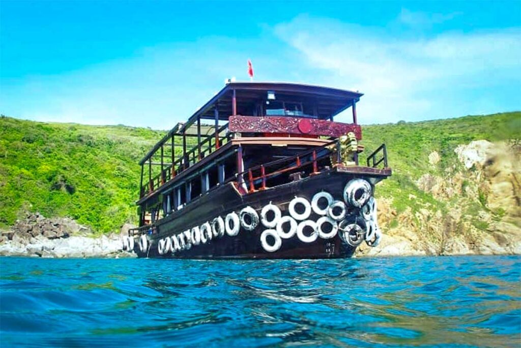 Hölzernes Tauchboot vor Anker vor einer felsigen Insel bei Nha Trang — Bootstauchen ist die übliche Möglichkeit, die Tauchplätze rund um Hon Mun und die anderen Inseln vor der Küste von Nha Trang zu erreichen