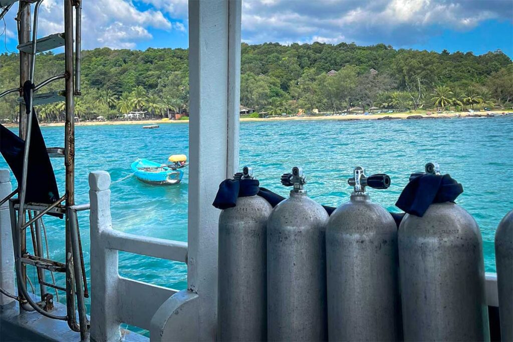 Reihe von Tauchflaschen auf dem Deck eines Tauchboots mit Blick auf das türkisfarbene Wasser und die grüne Küstenlinie von Phu Quoc — dies ist der Ausgangspunkt für jeden Tauchausflug, der von Phu Quoc zu den Inseln aufbricht