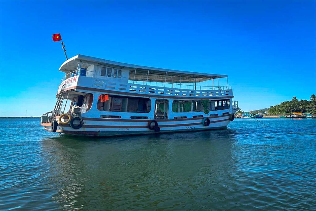 Zweistöckiges Tauchboot von Vietnam Active liegt im Hafen von Phu Quoc vor Anker mit Palmen und einem Strand im Hintergrund — Vietnam Active organisiert tägliche Tauchausflüge zu den besten Tauchstellen bei Phu Quoc