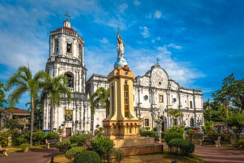 Koloniale spanisch-barocke Kathedrale in Cebu auf den Philippinen mit Glockenturm, weißer Steinfassade und einer Statue auf einem Monument davor