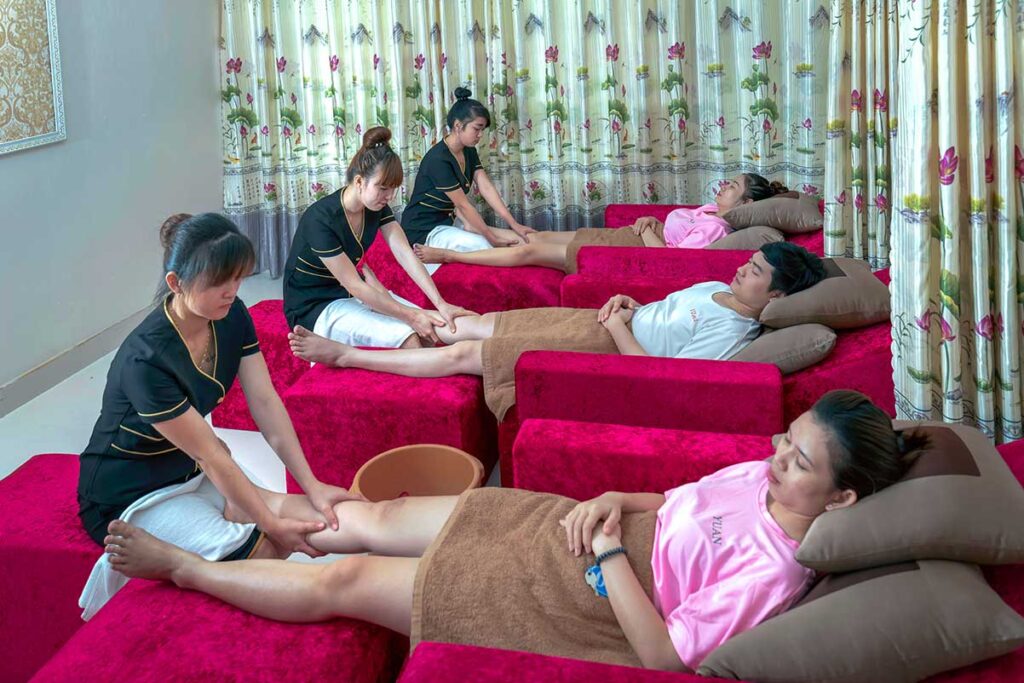 Drei Kunden liegen auf roten Betten während zwei vietnamesische Therapeuten eine Fußmassage in einem Massagesalon in Vietnam geben