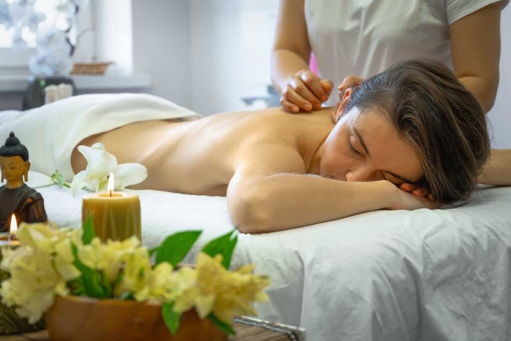 Frau erhält eine Ganzkörpermassage auf einem weißen Massagetisch in Vietnam, mit Kerzen und Blumen im Vordergrund