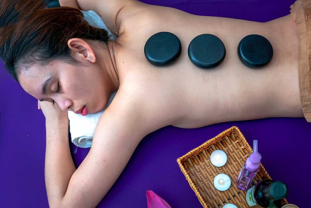 Frau erhält eine Ganzkörpermassage mit Kräuterstempel auf dem Rücken in einem vietnamesischen Spa, mit Kerzen und einer Buddhastatue im Vordergrund