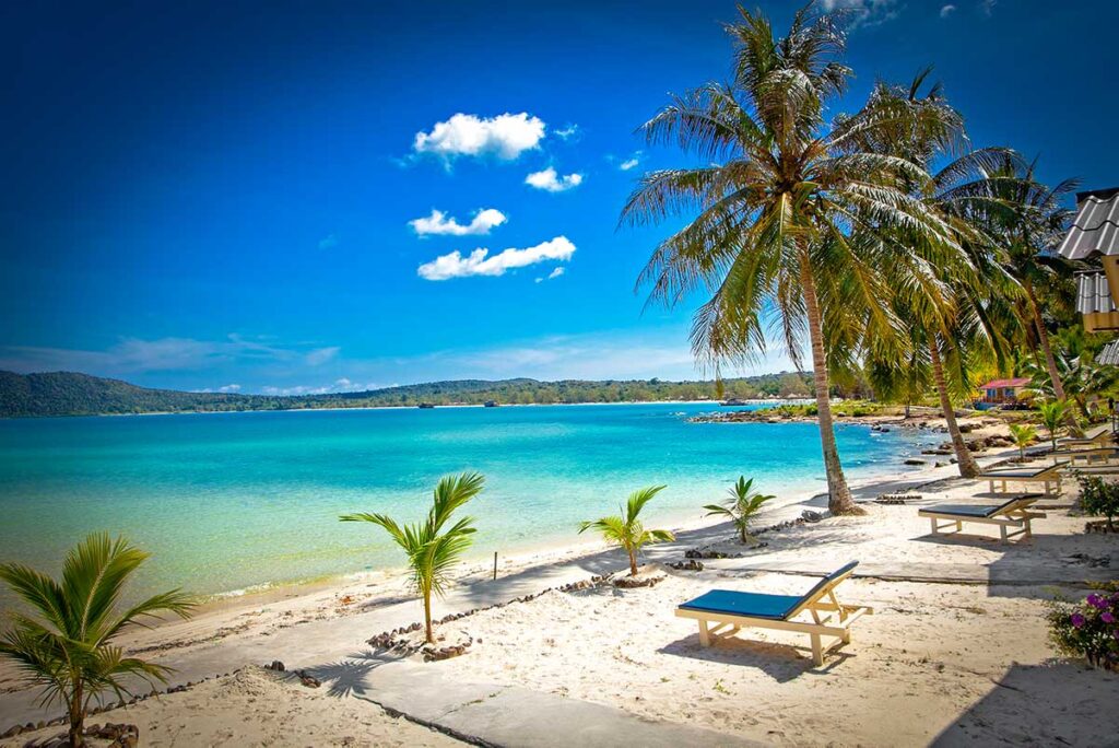 Weißer Sandstrand auf Koh Rong Samloem in Kambodscha mit türkisfarbenem Wasser, Palmen und Liegestühlen an einem sonnigen Tag