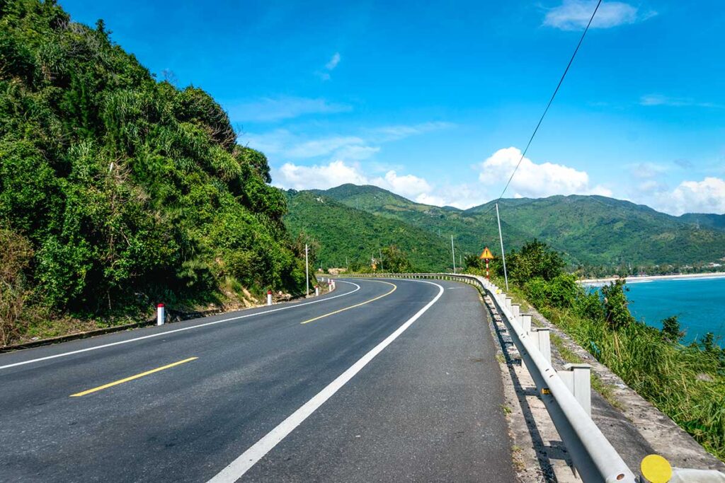 Leere Küstenstraße in Phu Yen, die sich entlang grüner Hügel auf der einen und türkisfarbenem Meer auf der anderen Seite schlängelt — die Küstenroute durch Phu Yen ist eine der schönsten Fahrstrecken in Zentralvietnam