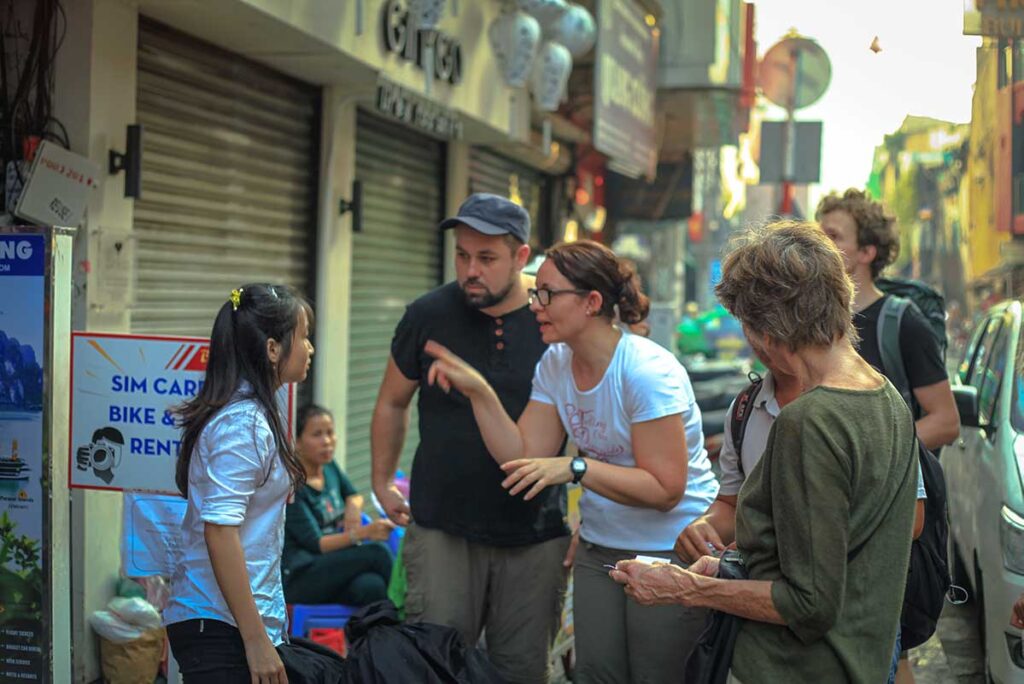 Westliche Reisende im Gespräch mit einem lokalen vietnamesischen Reiseführer auf der Straße, das Engagieren eines lokalen Guides ist eine der Möglichkeiten nachhaltig und verantwortungsvoll in Vietnam zu reisen