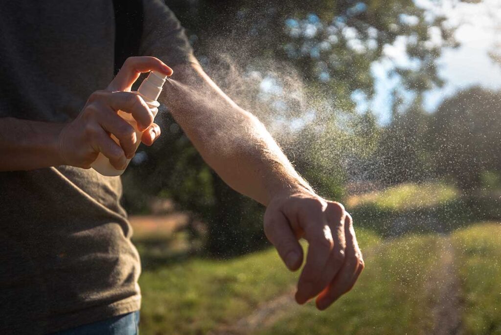 Person sprüht Insektenschutzmittel auf den Unterarm bei Sonnenuntergang im Freien — eine der wirksamsten Methoden zum Schutz vor Dengue in Vietnam