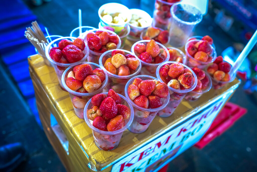 Reihe von Einwegplastikbechern mit Erdbeeren an einem Straßenstand in Vietnam, ein Beispiel des übermäßigen Plastikverbrauchs den nachhaltige Reisende in Vietnam im Blick haben