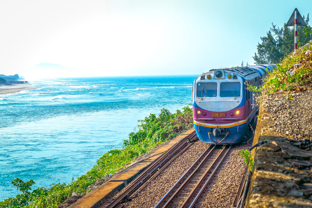 Vietnamesischer Zug fährt entlang der Küstenlinie mit türkisfarbenem Meer im Hintergrund, der Zug ist eine der nachhaltigsten und verantwortungsvollsten Arten durch Vietnam zu reisen