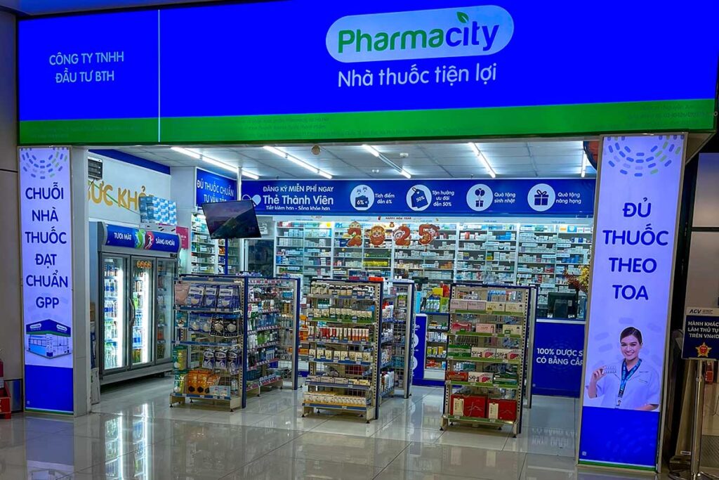 Filiale der Apothekenkette Pharmacity in Vietnam mit beleuchteter blauer Fassade und Regalen voller Medikamente