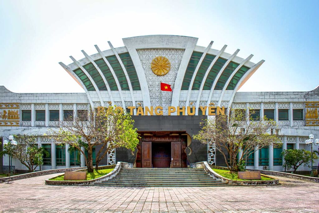 Frontansicht des Phu Yen Museums in Tuy Hoa mit einem auffälligen fächerförmigen Dach, vietnamesischer Fahne und breiten Eingangstreppen — das Museum bietet Informationen zur Geschichte und Kultur der Provinz