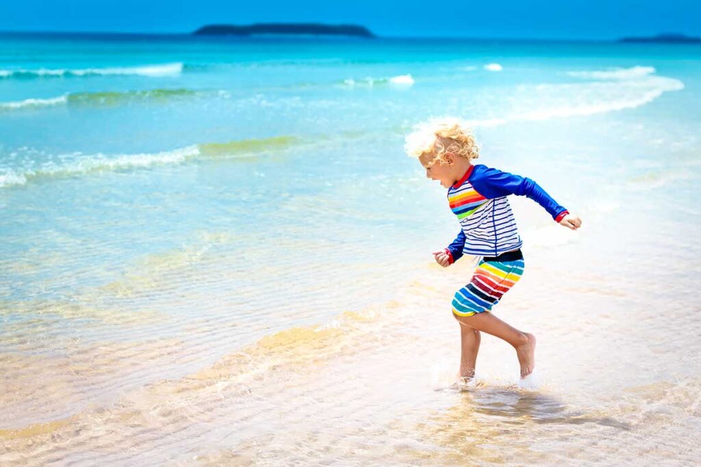 Kind in einem bunten Rashguard läuft durch das flache Wasser an einem Strand in Vietnam