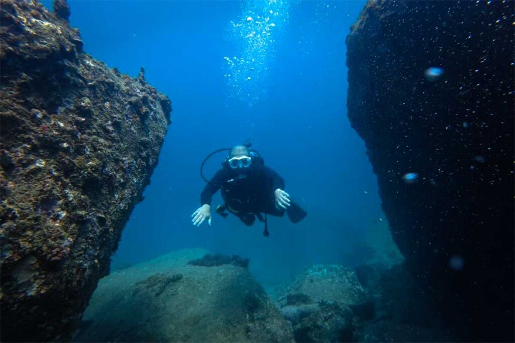 Scubataucher schwebt zwischen zwei großen Felsbrocken auf dem Meeresgrund bei Hon Mun, Nha Trang — die abwechslungsreichen Felsformationen machen Hon Mun zum beliebtesten Tauchgebiet bei Nha Trang