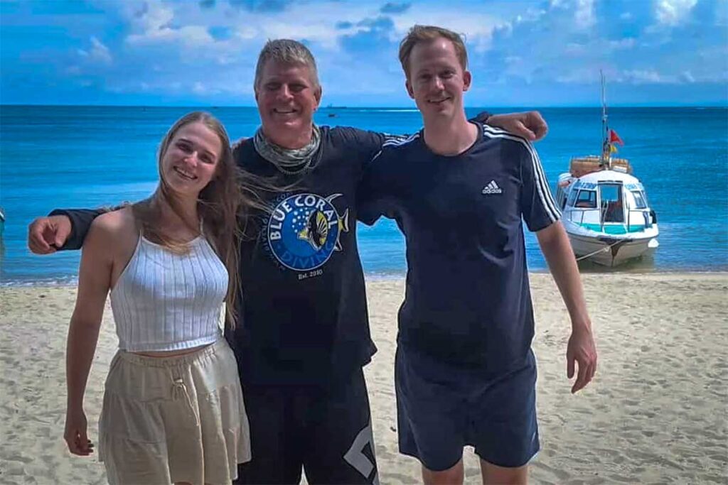 Tauchlehrer von Blue Coral Diving posiert mit zwei zufriedenen Kunden am Strand der Cham-Inseln — eine der bekanntesten Tauchschulen für alle, die bei Hoi An tauchen möchten