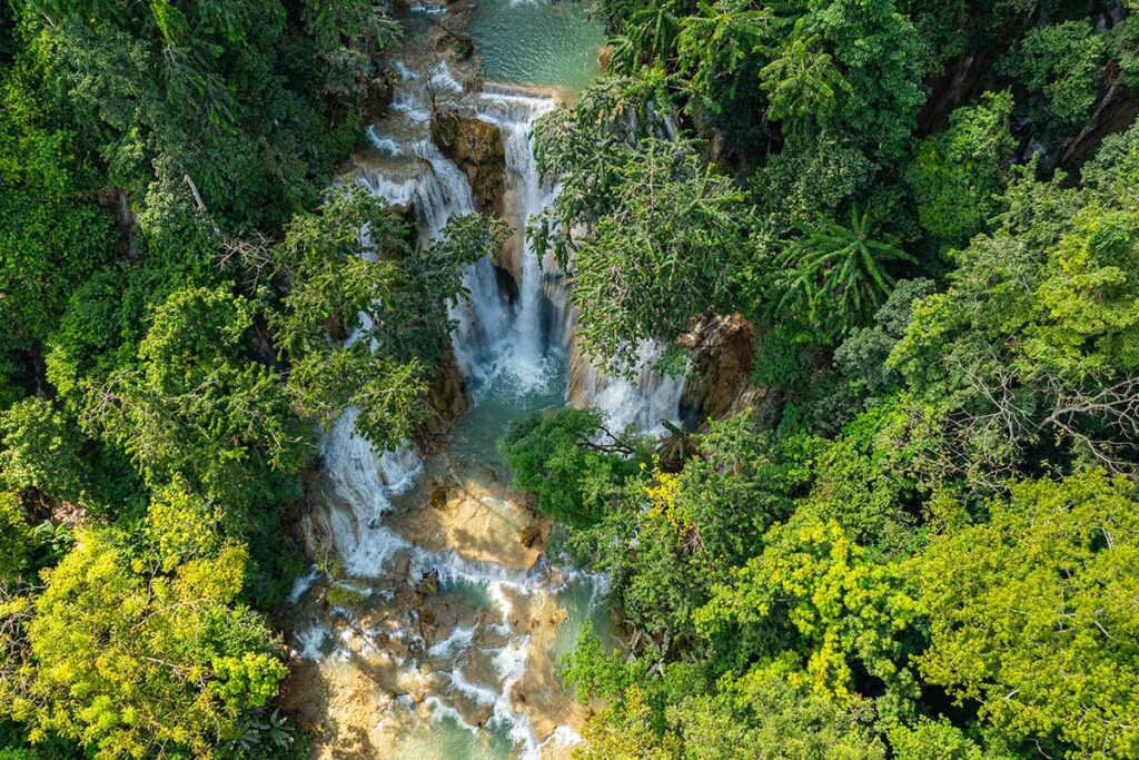 Luftaufnahme der Tat-Kuang-Si-Wasserfälle bei Luang Prabang in Laos, mit mehreren Stufen türkisfarbenen Wassers umgeben von dichtem tropischem Regenwald