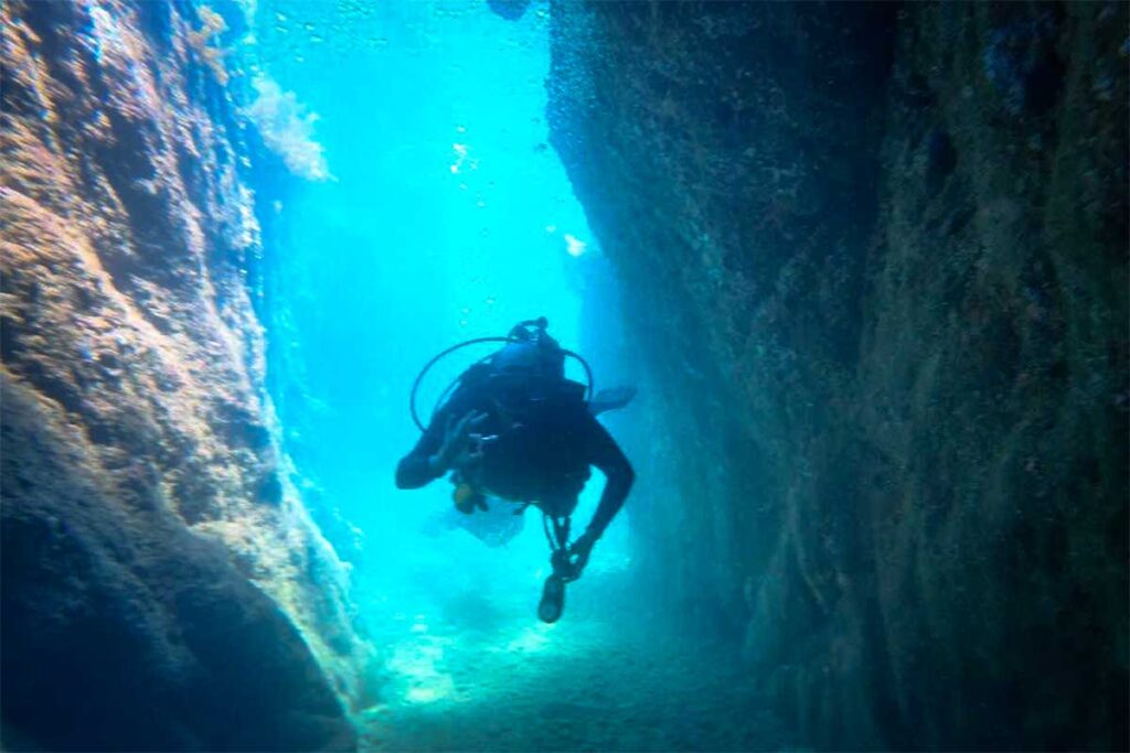 Scubataucher schwimmt durch eine enge Unterwasserschlucht mit blauen Felswänden bei Nha Trang — die Schlucht bei Hon Mun gilt als eine der interessantesten Tauchstellen für fortgeschrittene Taucher in der Region