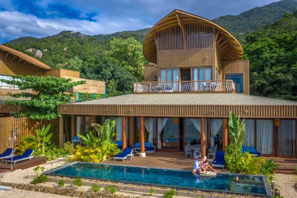 Villa des An Lam Retreats Ninh Van Bay mit geschwungenem Holzdach, Privatpool und Liegestühlen auf einer Terrasse, umgeben von tropischem Garten und Bergen — eines der luxuriösen Unterkünfte in der Bucht