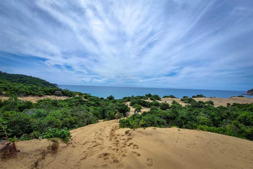 Blick von einer Sanddüne auf der Dam Mon Halbinsel über die Van Phong Bay, mit Besuchern im Bewuchs und dem Meer im Hintergrund — ein unbekannter, aber eindrucksvoller Ort