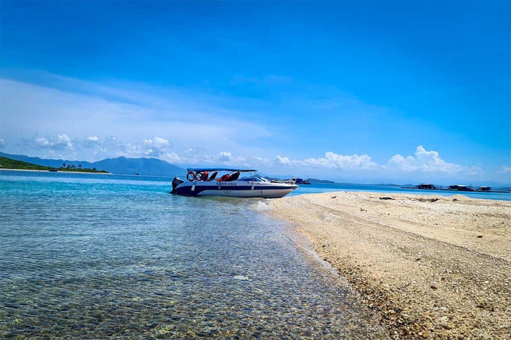 Schnellboot am Ufer einer schmalen Sandbank in der Van Phong Bay mit klarem flachem Wasser und Inseln im Hintergrund — Schnellboottouren verbinden die Inseln der Bucht