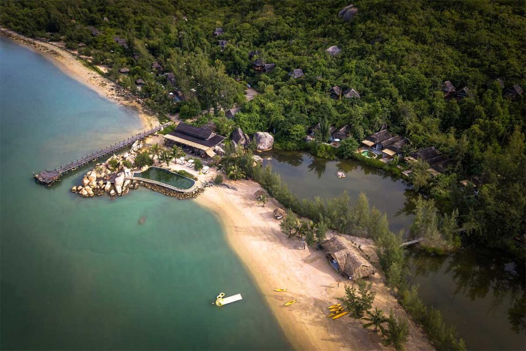 Luftaufnahme des Lalya Resorts in der Ninh Van Bay mit Reetbungalows verteilt im Dschungel, einem Pool neben den Felsen, einem Sandstrand und gelben Kajaks bereit zur Nutzung