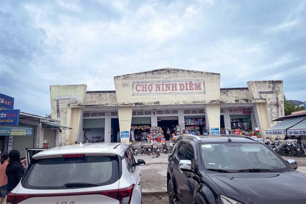 Außenansicht des Cho Ninh Diem Marktes in Ninh Thuy bei Doc Let Beach, ein lokaler Markt mit einem alten Betonmarktgebäude und Betrieb vor dem Eingang