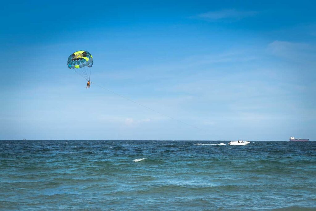 Parasailer hängt hoch über dem Meer bei Doc Let Beach an einem bunten Fallschirm, mit einem Schnellboot auf dem Wasser — Parasailing ist eine der Wassersportaktivitäten bei Doc Let
