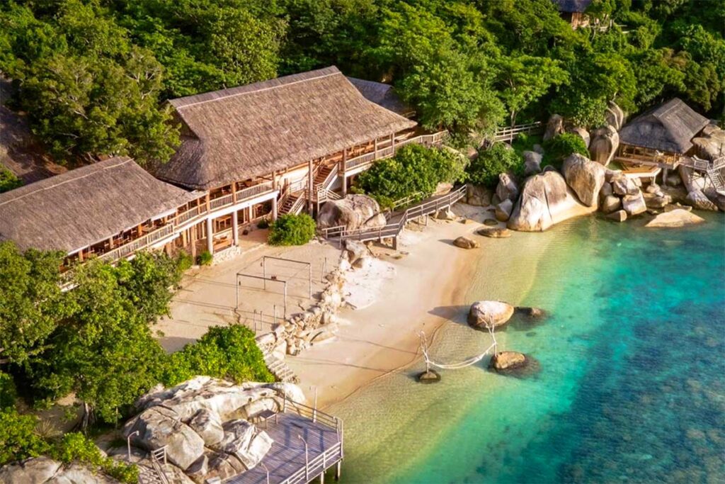 Luftaufnahme des Six Senses Resorts in der Ninh Van Bay mit Reetbungalows versteckt zwischen Felsen und Dschungel, einem Pool direkt am Wasser und einem Holzsteg — nur per Boot erreichbar