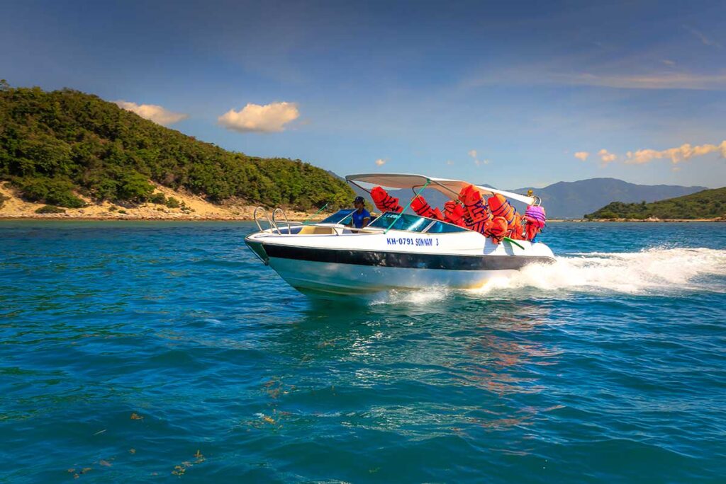 Schnellboot mit orangefarbenen Schwimmwesten fährt durch das blaue Wasser entlang grüner Hügel bei Diep Son — Schnellboottouren zu Diep Son starten aus der Gegend von Doc Let Beach