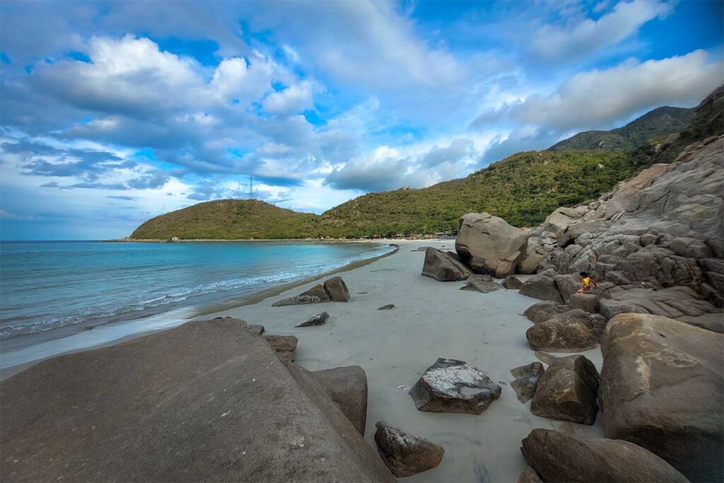 Verlassener Strand auf der Hon Heo Halbinsel in der Van Phong Bay mit großen Felsbrocken auf dem weißen Sand, grün bewaldeten Hügeln und hellblauem Wasser — kaum touristisch und schwer zugänglich